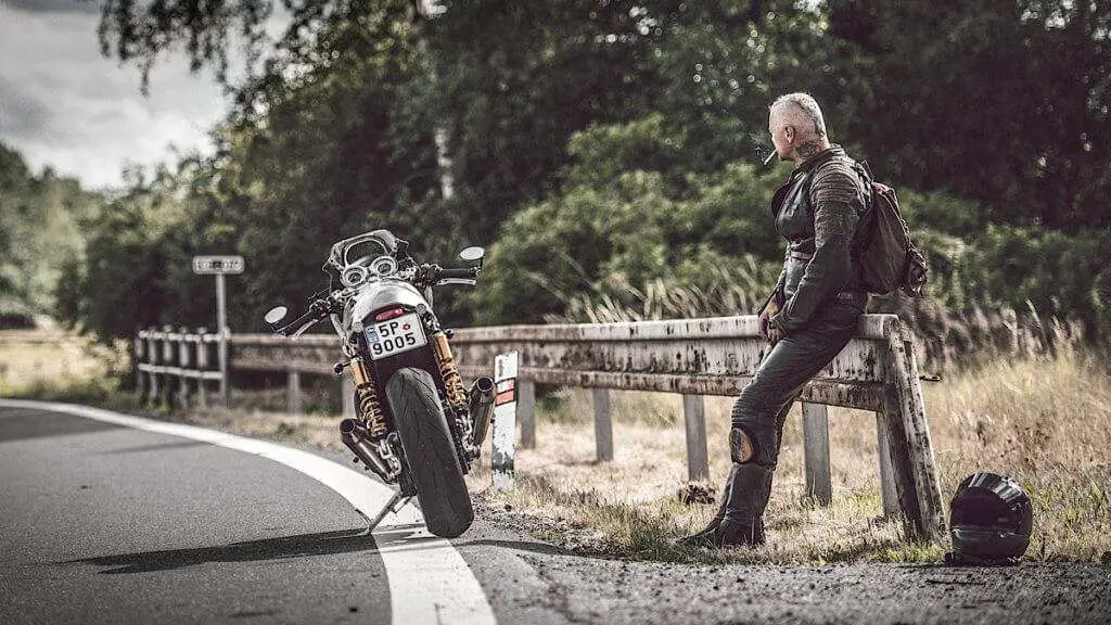 Man on the side of the road next to a motorcycle