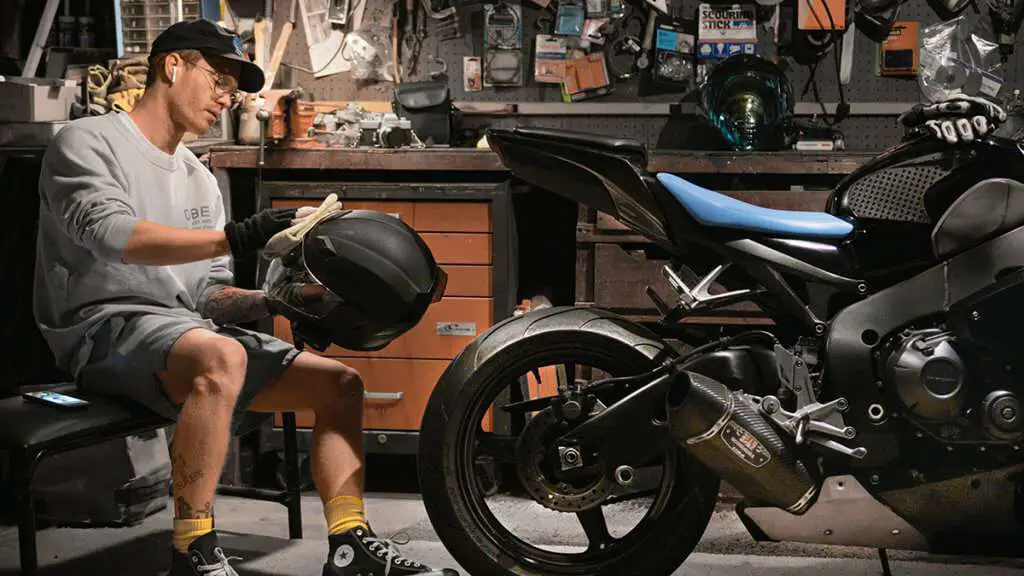 Man cleaning this motorcycle helmet in a garage next to a motorcycle