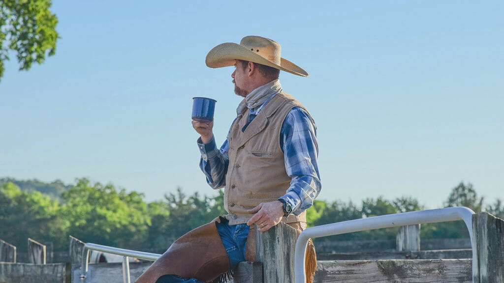 Cowboy wearing chaps and drinking from a cup