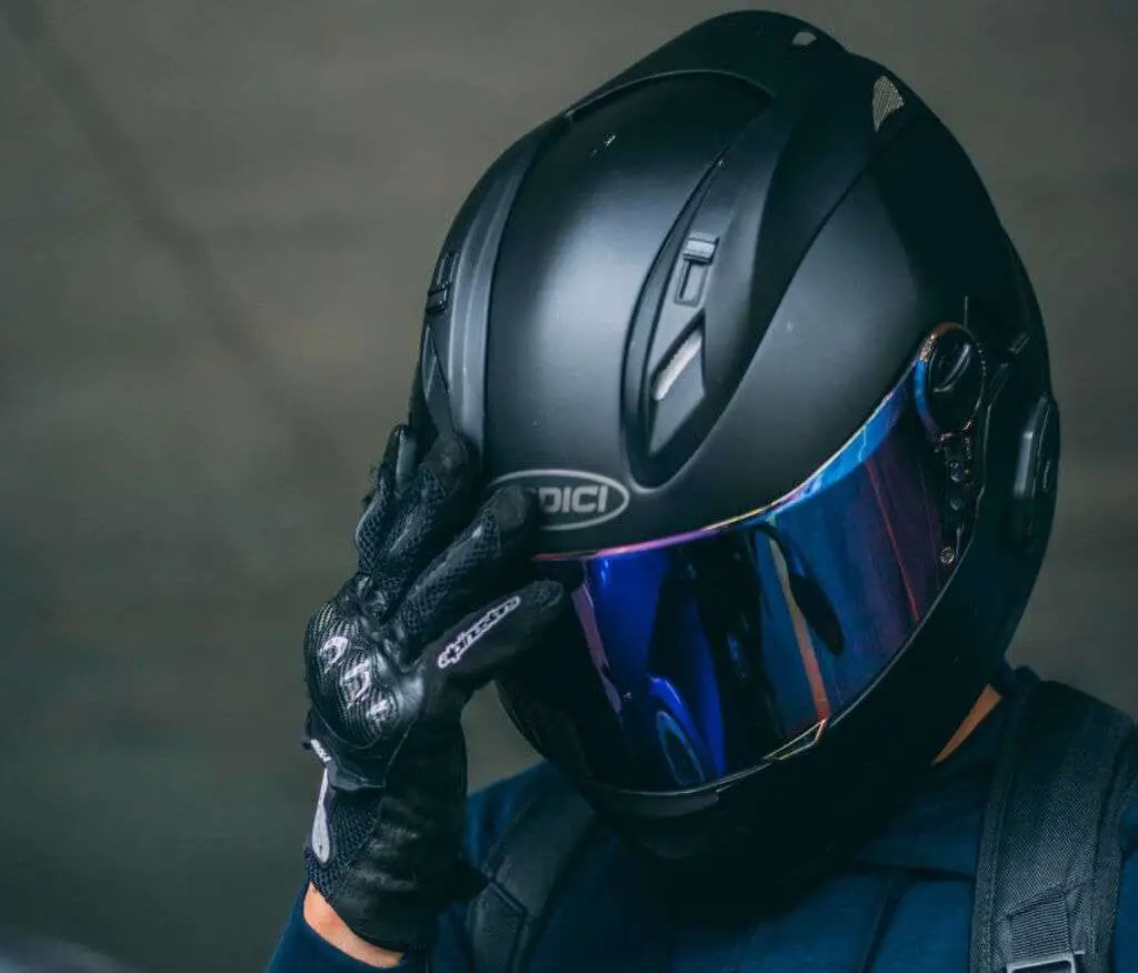 Person with black motorcycle helmet holding hand on the visor