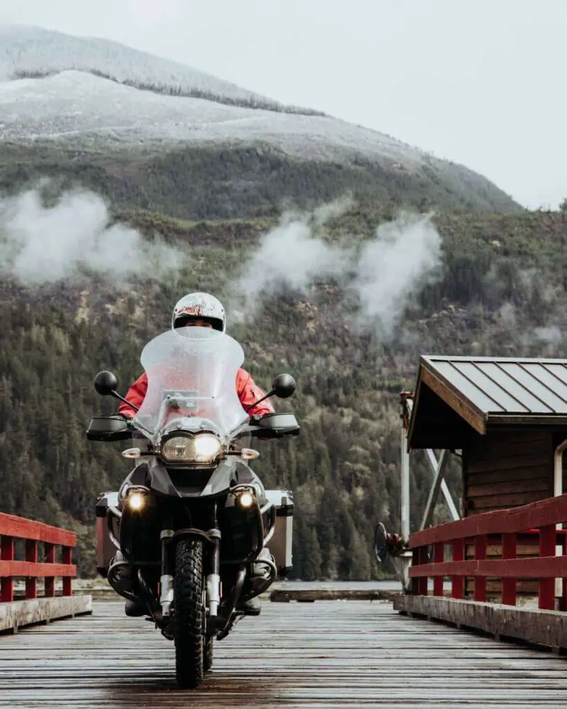 Person riding an adventure motorcycle on a wet bridge with clouds above