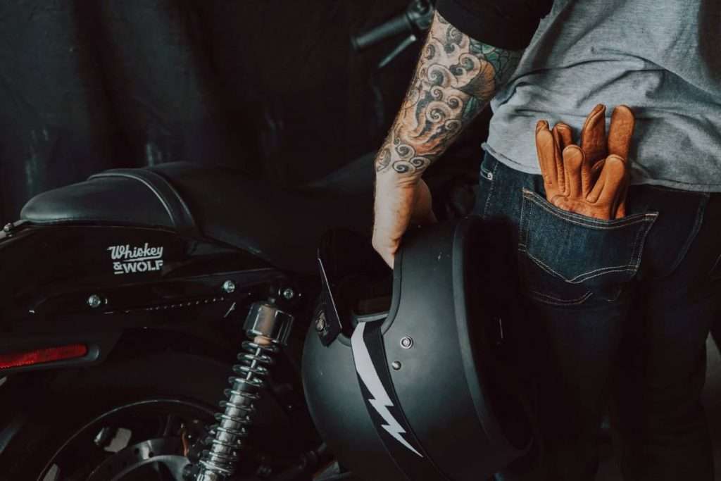 Man holding a motorcycle helmet with brown gloves in the back pocket